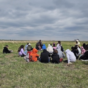 children sitting on grass facing a man 