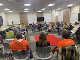 group of people sitting in a circle with a red blanket on the floor in the middle